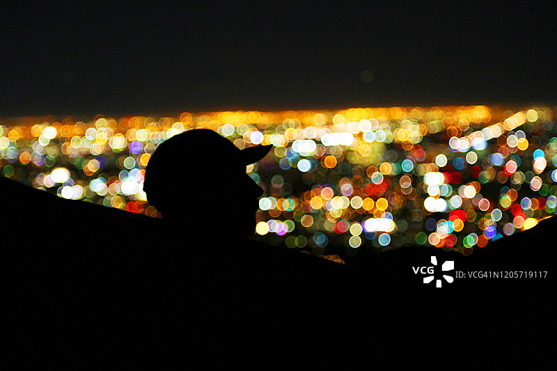 戴棒球帽的男子在吊床上看城市夜景的轮廓图片素材