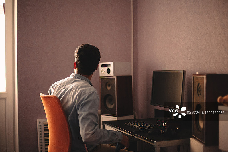 男人在家中坐在电脑旁，透过窗户观察图片素材