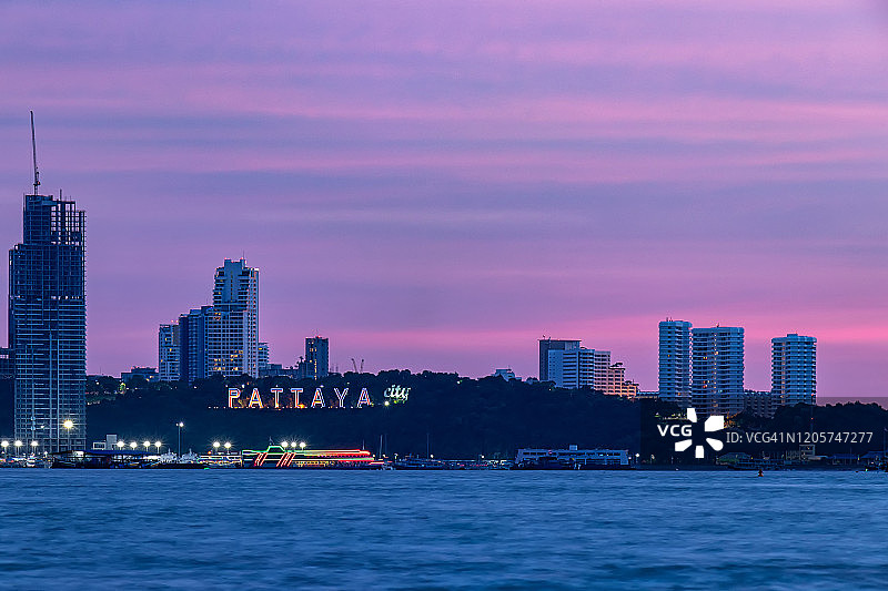 芭堤雅海湾城市标志，夜晚在山顶观景点发光，前景是海，船在海上漂浮图片素材