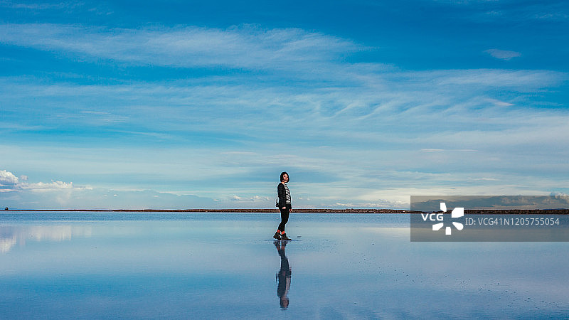 在乌尤尼盐湖的盐滩上对着天空行走的女人图片素材
