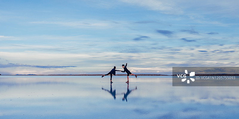 情侣在乌尤尼盐沼的盐滩上对着天空跳舞图片素材