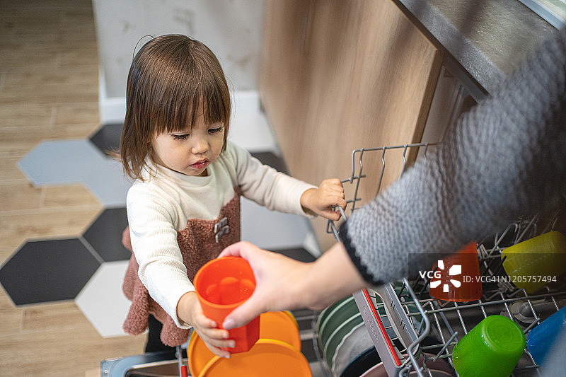 可爱的幼儿帮助她的母亲将餐具放入洗碗机图片素材
