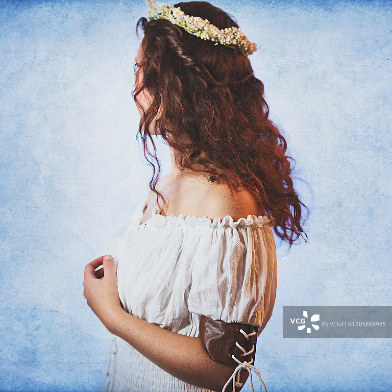 长波浪红发年轻女子的背影，穿着露肩女衫，头戴花冠，蓝色背景图片素材