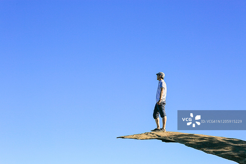 男人站在加州伍德森山顶的薯片岩上，背景是蓝天图片素材