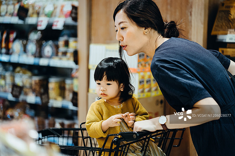 母亲推着装有小女儿的购物车在超市里购买食品图片素材
