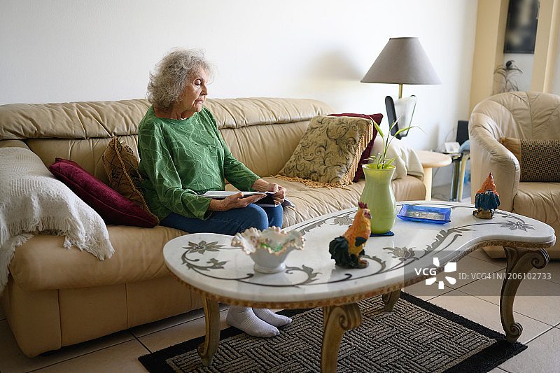 80多岁的年长女性在客厅里看杂志图片素材