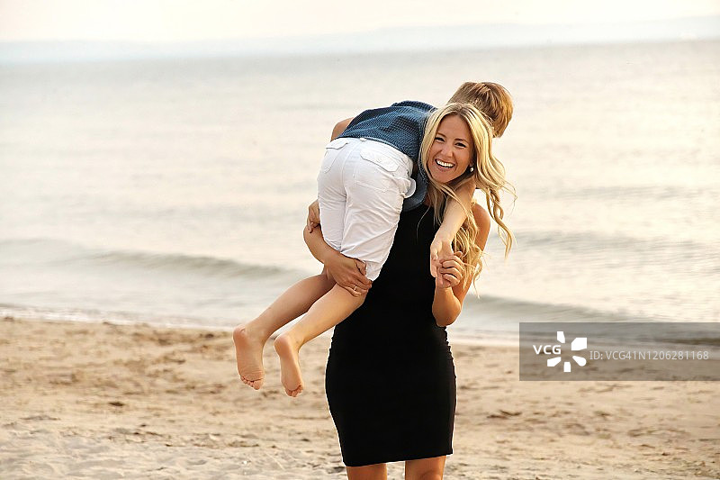 年轻的母亲在海滩上嬉戏地将儿子举过肩头的真实瞬间图片素材