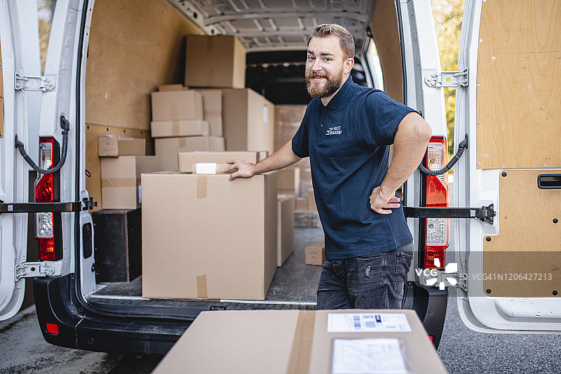 微笑的男快递员将包裹装载到货车上图片素材