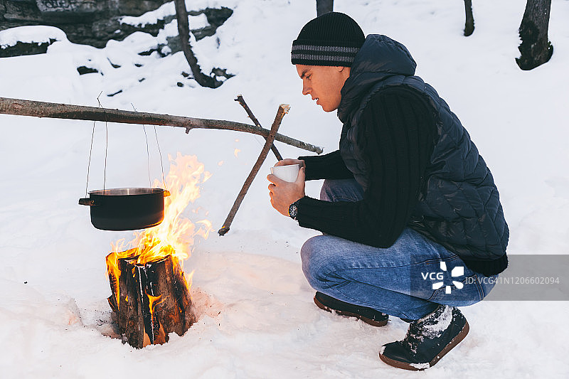 冬季露营：男人双手取暖，锅中烧水，荒野雪景图片素材