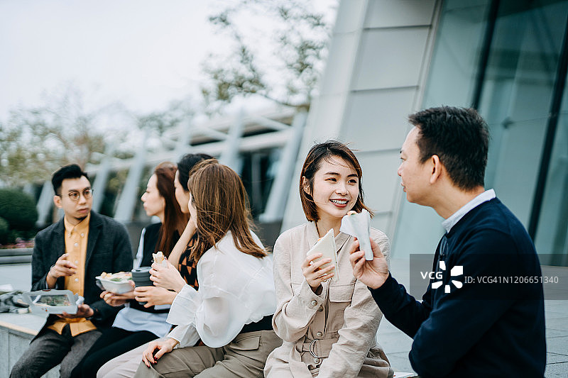 一群亚洲商业伙伴在城市阳台上共进午餐，享受美好时光，他们聊天并分享食物图片素材