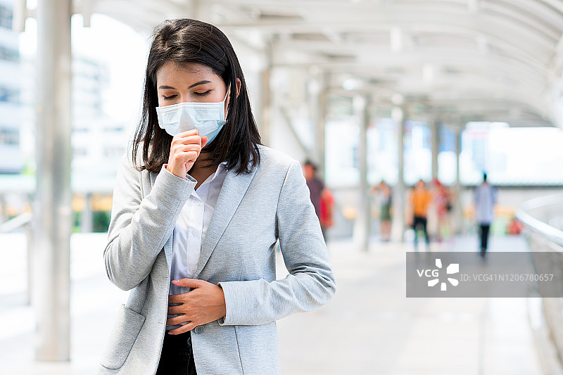 户外站立，佩戴口罩并咳嗽的亚洲女性图片素材