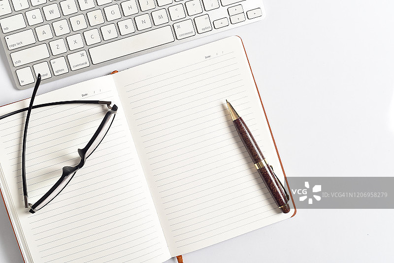 白色木质办公桌顶部视图，配有电脑键盘、笔、记事本图片素材