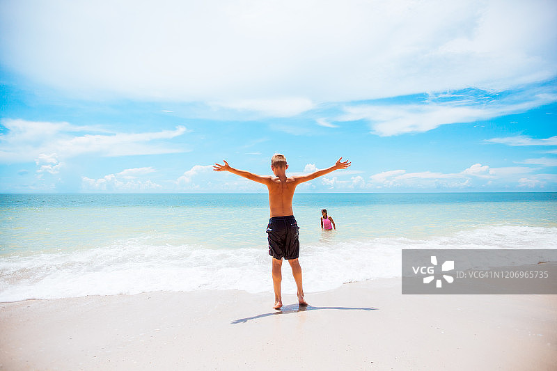 男孩在水边张开双臂，妹妹在海里玩耍图片素材