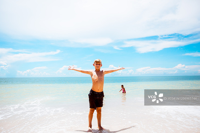 男孩在水边张开双臂，妹妹在海里玩耍图片素材