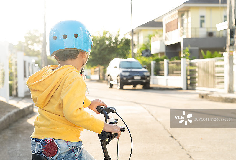 戴安全帽骑自行车的微笑男孩，夏季在沥青路上的亚洲儿童图片素材