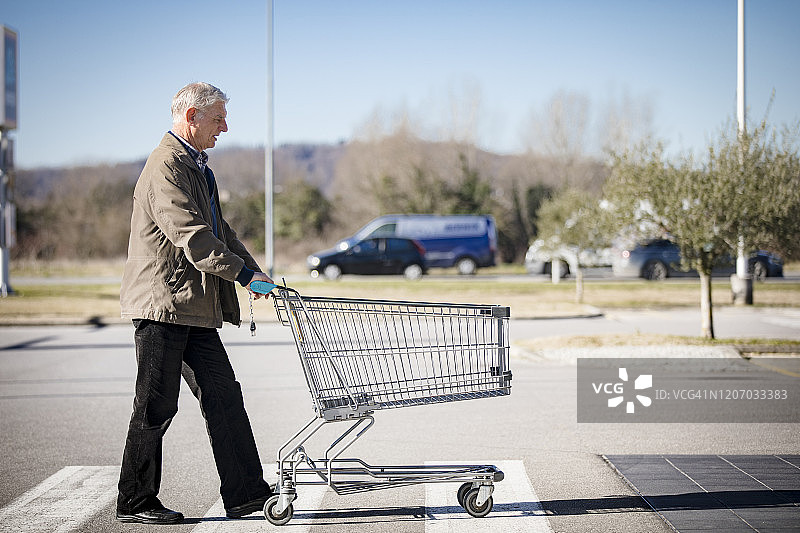年长的男人在超市停车场推着空购物车图片素材