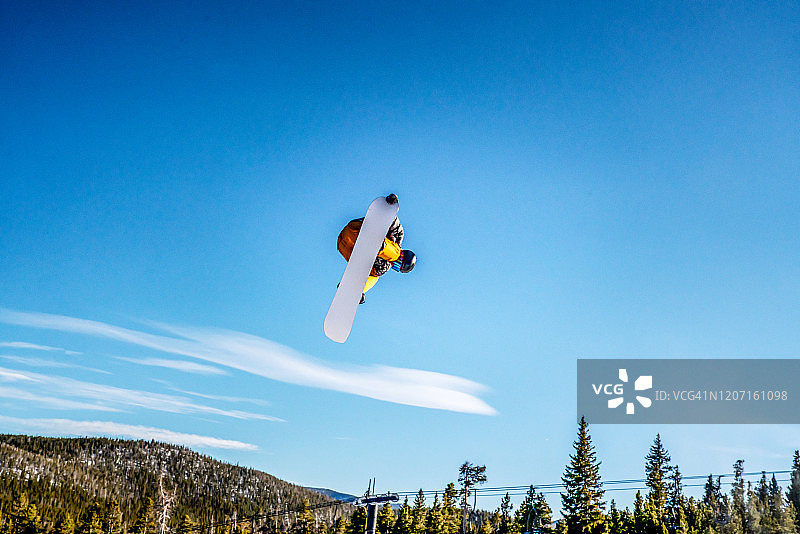 在阳光明媚的日子里，一位年轻的男性单板滑雪者在科罗拉多州滑雪区跳跃图片素材