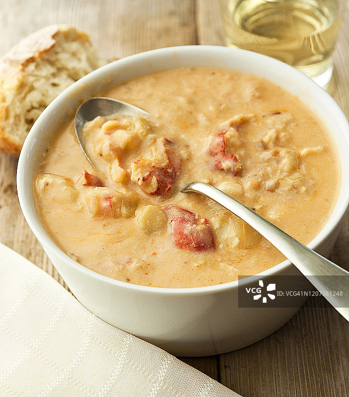 乡村木桌上的龙虾浓汤配酒、面包、勺子和餐巾图片素材