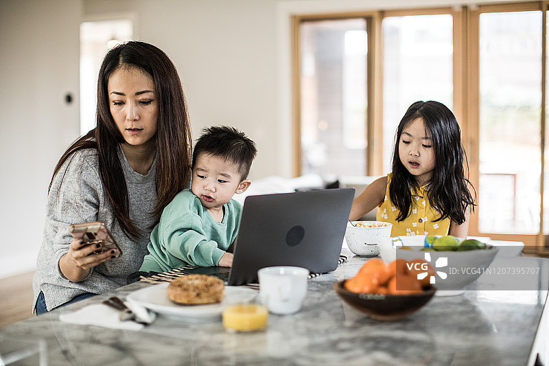 母亲在厨房的餐桌上照顾年幼的孩子们图片素材