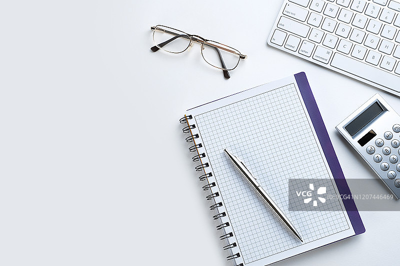 打开的笔记本上的笔，旁边是计算器、眼镜和笔记本电脑。商人或会计师物品旁的空白笔记本纸，财务报告概念。图片素材
