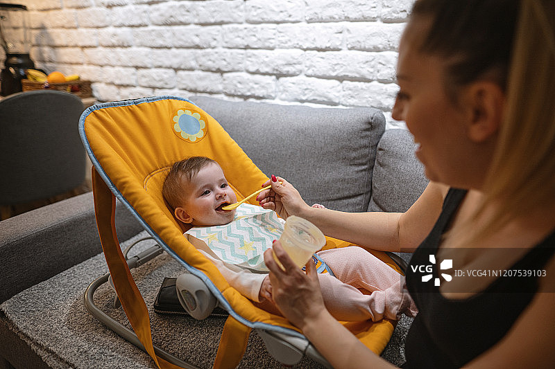 温馨母亲照顾小女婴，喂食胡萝卜泥图片素材