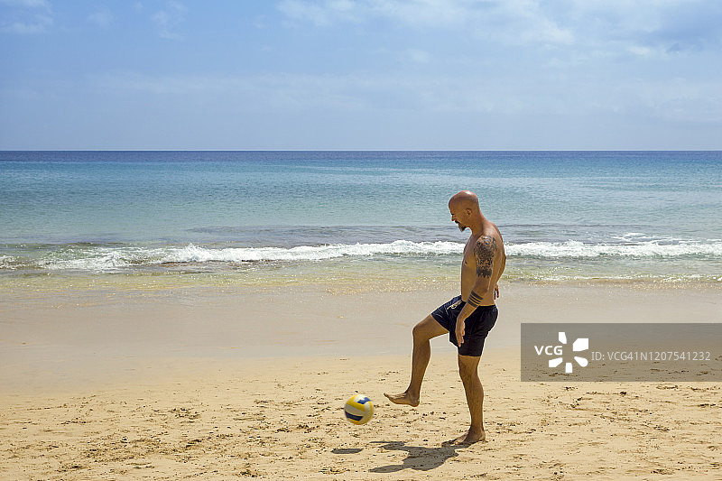 男人在沙滩上踢足球图片素材