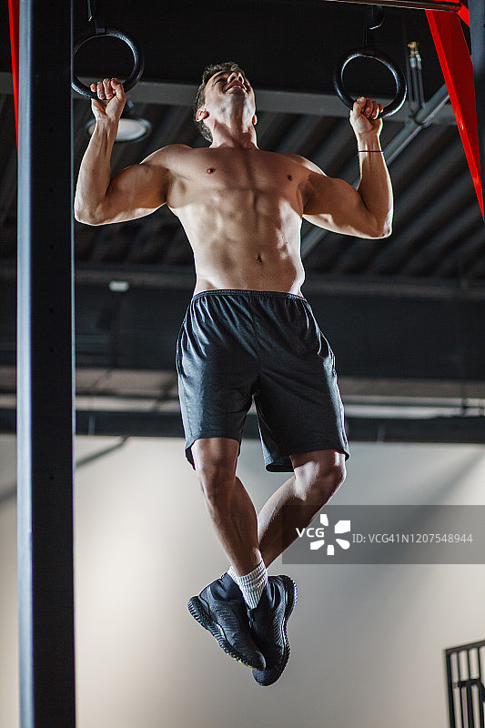 在健身房的体操吊环上做引体向上的健壮男人图片素材