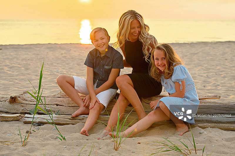一家人在日落时坐在海滩上的浮木上的真实生活肖像图片素材