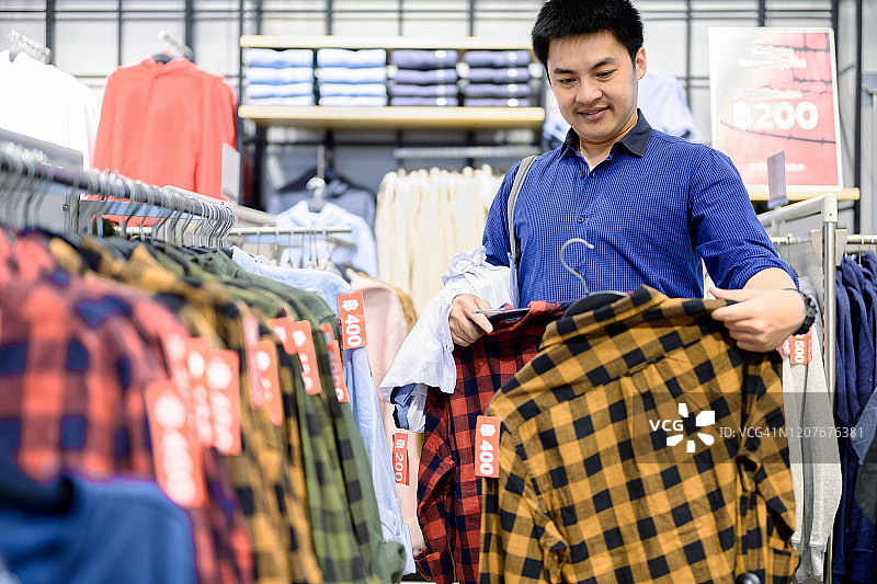 在购物中心服装店挑选衣服的亚洲男职员，比较衬衫的差异，时尚和消费概念图片素材