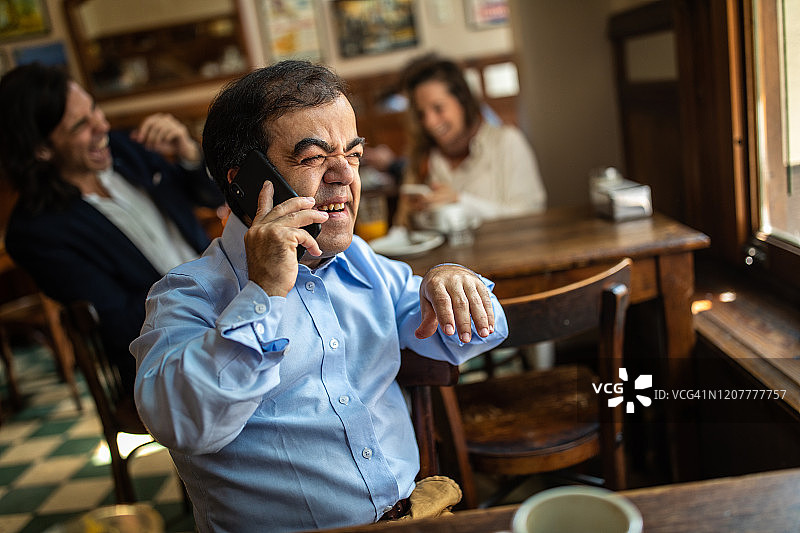 独自坐在咖啡馆使用智能手机的患有侏儒症的中年男人图片素材