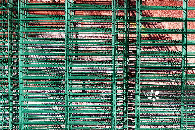 阳光明媚的户外，建筑墙背景上的金属网链绿色围栏图片素材