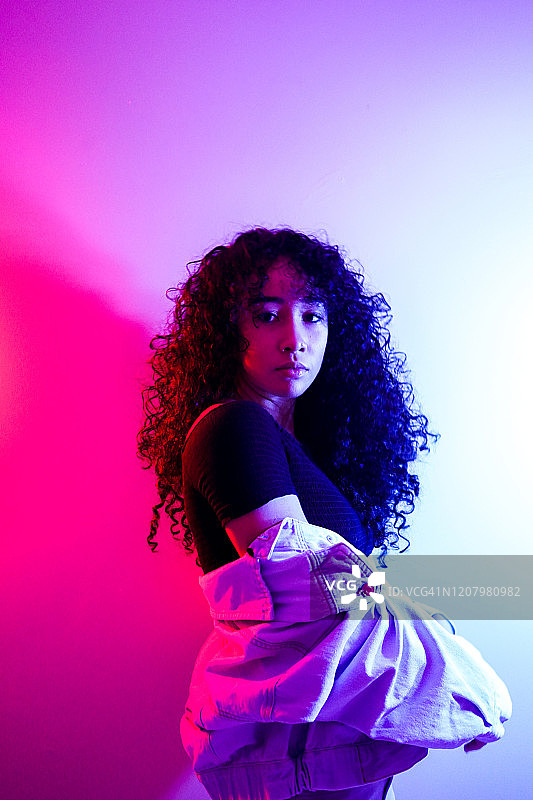 年轻女人靠在粉色墙壁上，看着镜头图片素材