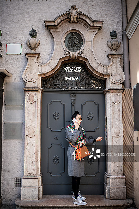 女子在传统建筑入口前使用对讲机和手机交谈图片素材