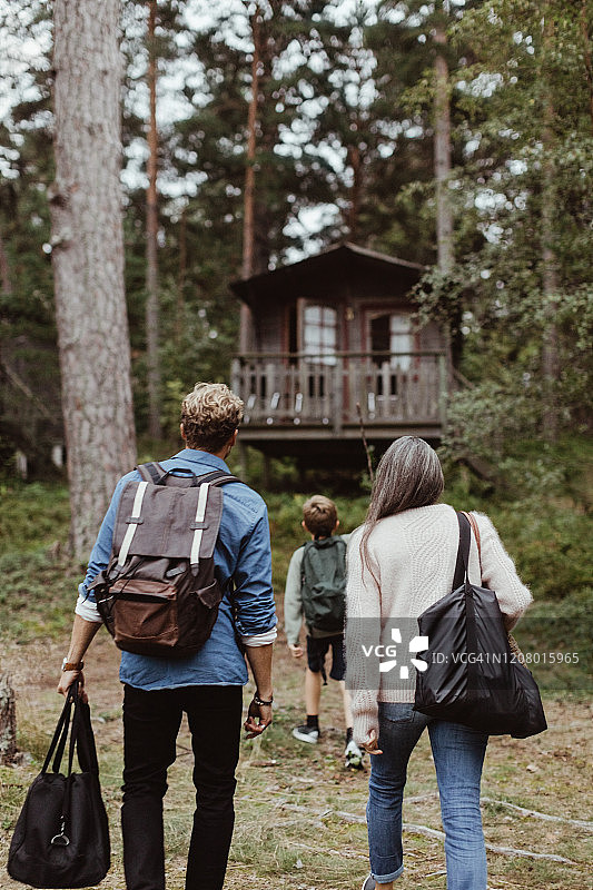 带着行李走向森林房子的家庭后视图图片素材
