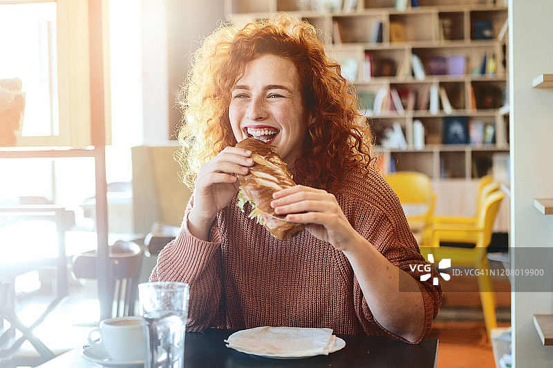 年轻的红发女子咬着美味的三明治图片素材