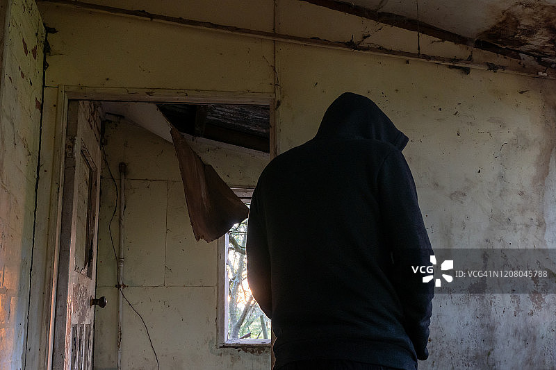 仰望废弃房屋中戴兜帽的神秘人物的背影（黑暗氛围）图片素材