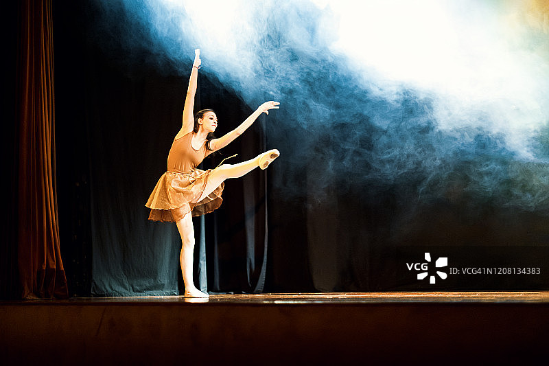 年轻女孩在蓝色烟雾的黑暗舞台上跳芭蕾舞图片素材