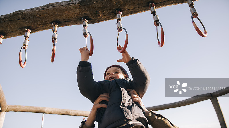 父亲托起男孩抓握室外体操吊环的手部细节图片素材