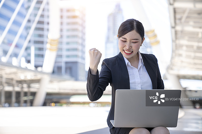 兴奋的亚洲女性看着笔记本电脑屏幕，庆祝工作场所的成功，为收到好消息感到高兴，感到兴奋，在线获胜，获得绝佳的报价或机会图片素材