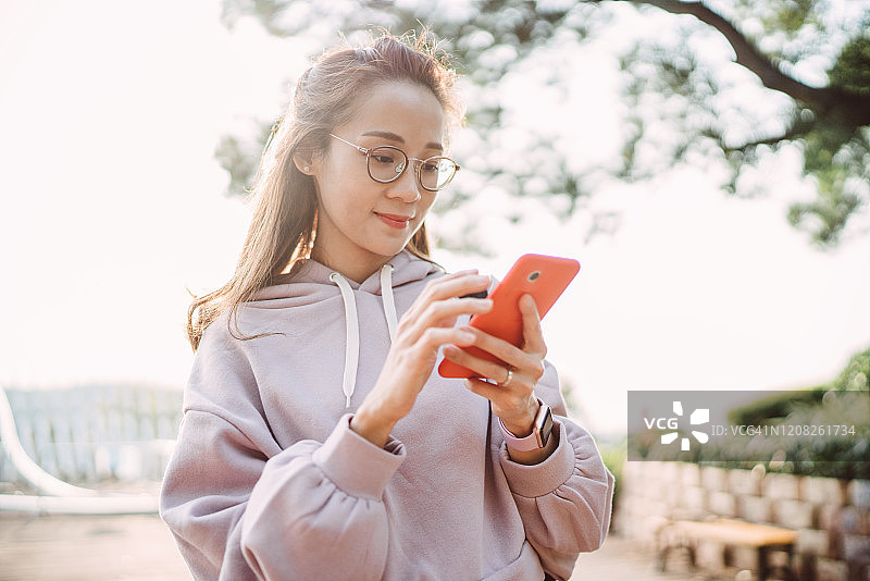 在公园里愉快地使用智能手机的亚洲年轻女士图片素材