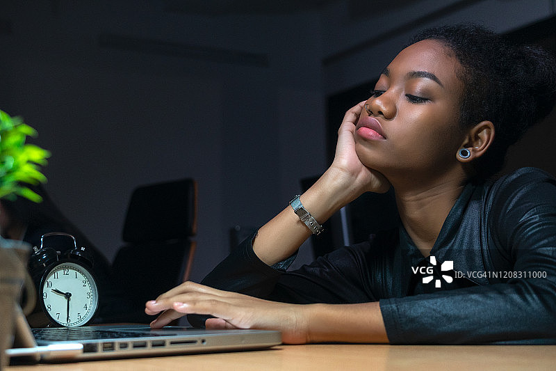 年轻女商人在现代办公室的办公桌前工作，看起来很无聊图片素材