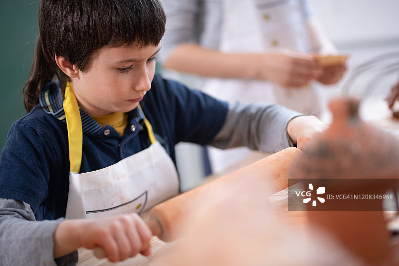 年轻的男学生用擀面杖压平黏土图片素材