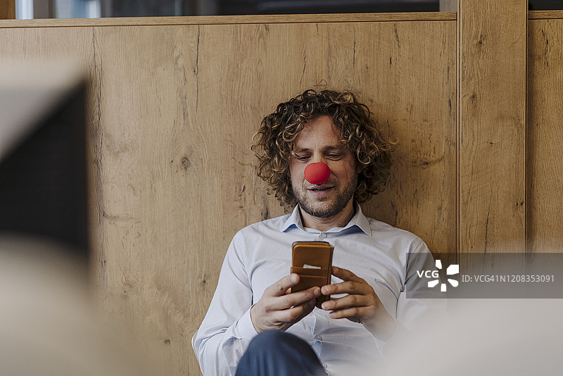 在办公室里戴着红色小丑鼻子的商人使用手机图片素材