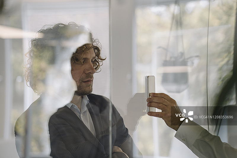 商人隔着玻璃窗向同事展示手机图片素材