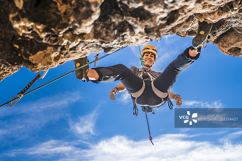 微笑的女登山者从岩壁上绳降的肖像图片素材