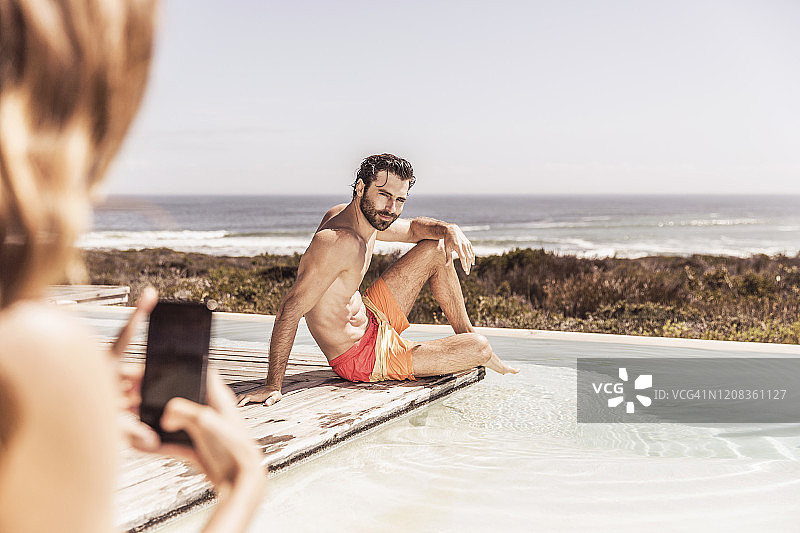 女人在泳池边用智能手机拍摄年轻男人图片素材