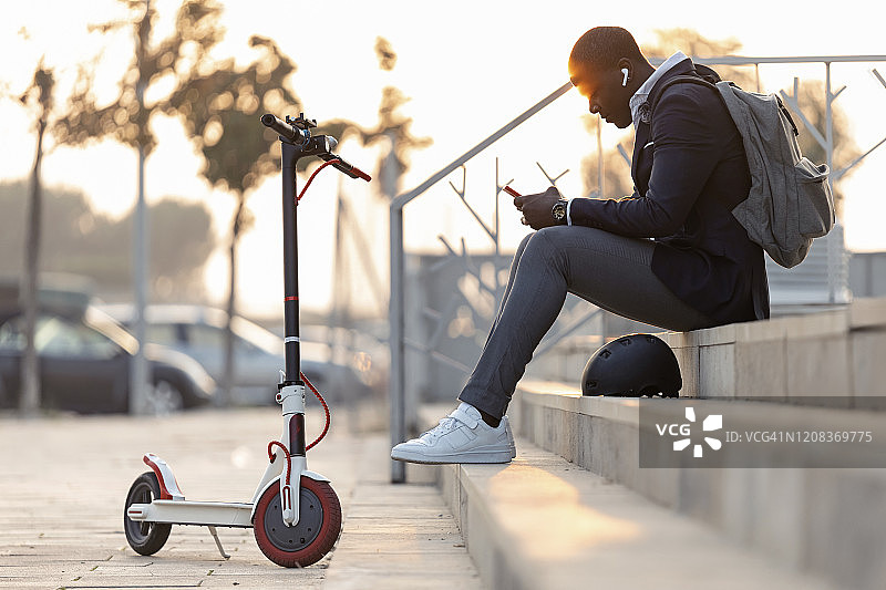 年轻商人傍晚坐在楼梯上，使用手机和耳机图片素材