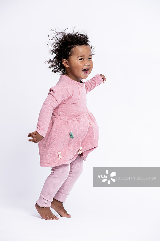 赤脚粉衣小女孩在白色背景前跳跃的肖像图片素材