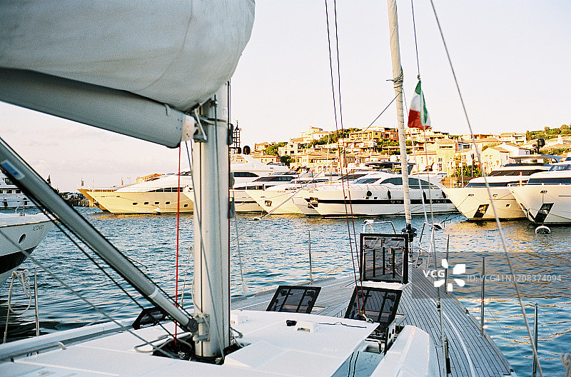 从停泊在撒丁岛切尔沃港的白色帆船游艇船头看到的日落景色图片素材