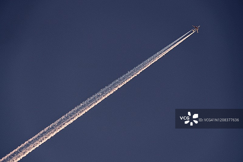 蓝色天空中的飞机尾迹与黎明时分的阳光倒影图片素材